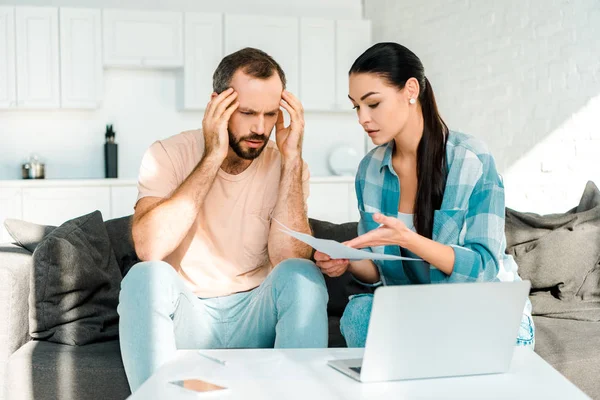 Casal estressado sentado no sofá, usando laptop e tendo problemas financeiros — Fotografia de Stock