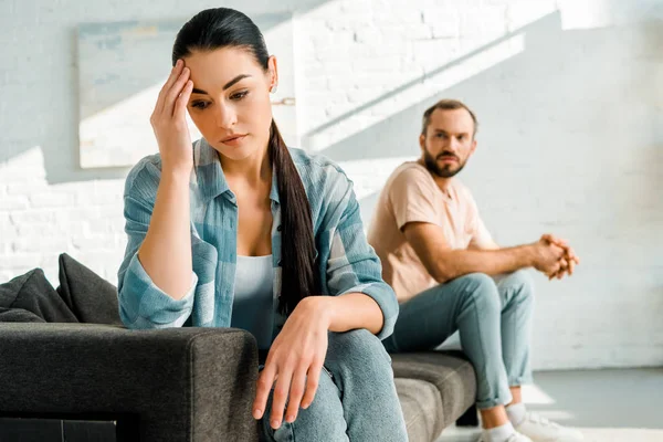 Traurige Frau mit Hand auf dem Kopf sitzt nach Streit mit Ehemann zu Hause im Vordergrund — Stockfoto