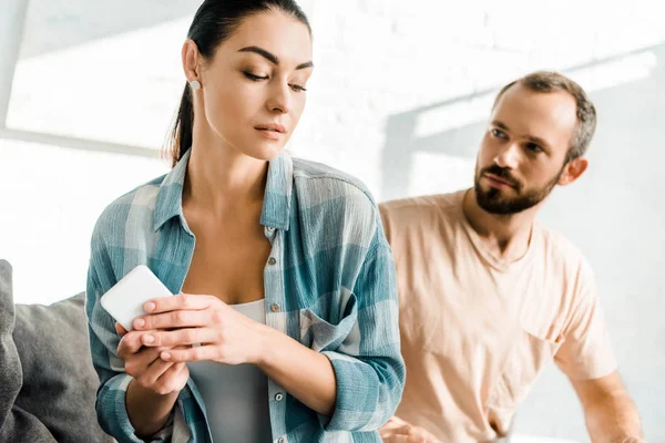 Esposa sosteniendo el teléfono inteligente y tener malentendidos con el marido en casa — Stock Photo