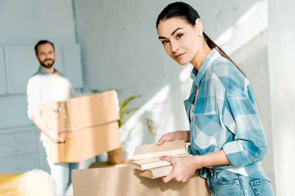 Beautiful wife putting books in cardboard box while husband holding cardboard boxes, moving concept — Stock Photo