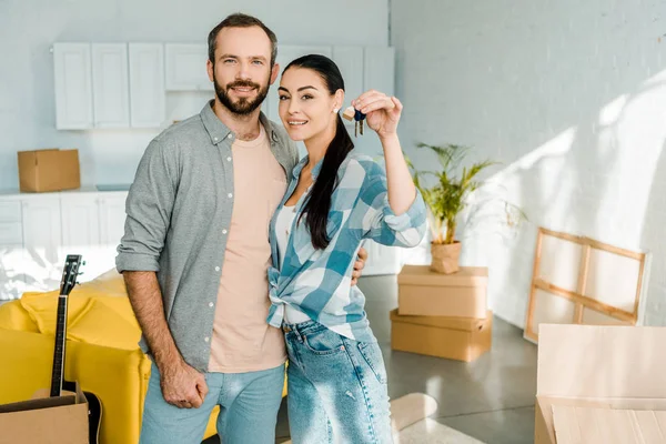 Smiling couple looking at camera and wife holding keys from new house, moving concept — Stock Photo