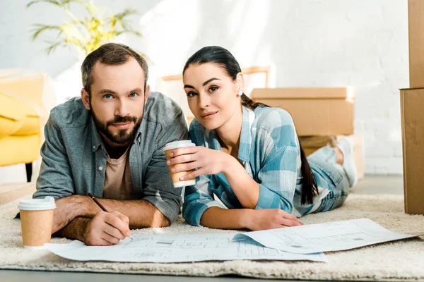 Mann und schöne Frau liegen auf dem Boden, trinken Kaffee und arbeiten zu Hause an Entwürfen für ein neues Haus, bewegendes Konzept — Stockfoto