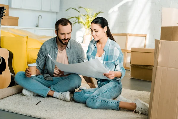 Beautiful couple drinking coffeeand holding blueprint of new house, moving concept — Stock Photo