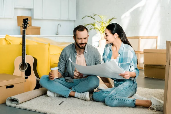 Felice marito e moglie bere caffè e tenendo cianografia della nuova casa, concetto in movimento — Foto stock