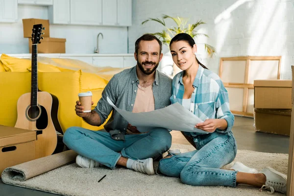 Bonito marido e mulher beber café e segurando planta da casa nova, conceito em movimento — Fotografia de Stock