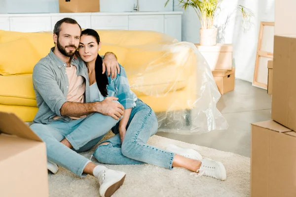 Hermosa pareja sentada en el suelo, abrazándose y relajándose después de empacar para una nueva casa, concepto móvil - foto de stock
