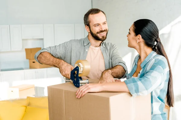 Husband and wife packing cardboard box with scotch tape, moving concept — Stock Photo