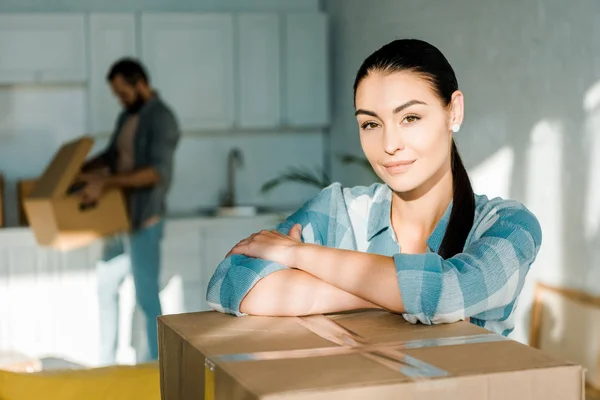 Hermosa esposa mirando a la cámara en primer plano con el marido detrás de embalaje para la nueva casa, concepto en movimiento - foto de stock