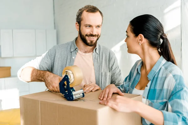 Husband and wife packing cardboard box with scotch tape, moving concept — Stock Photo