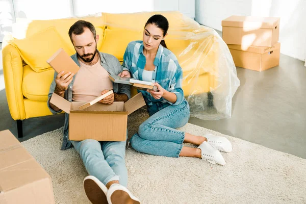 Beautiful couple putting books in cardboard box while packing for new house, moving concept — Stock Photo