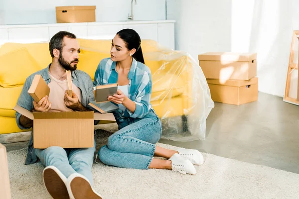 Serious couple putting books in cardboard box while packing for new house, moving concept — Stock Photo