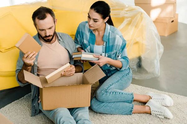 Belo casal colocando livros em caixa de papelão ao embalar para nova casa, conceito em movimento — Fotografia de Stock