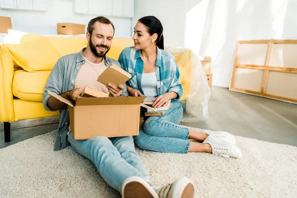 Happy couple putting books in cardboard box while packing for new house, moving concept — Stock Photo