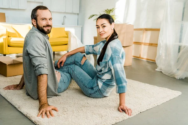 Sonrientes marido y mujer sentados en el suelo y descansando después de empacar para una nueva casa, concepto móvil - foto de stock