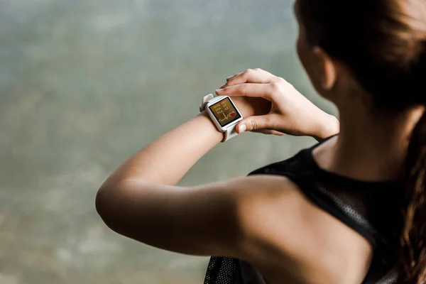 Ausgeschnittene Ansicht einer Sportlerin beim Betrachten einer Sport-Smartwatch, die die Herzschlagrate im Fitnessstudio zeigt — Stockfoto