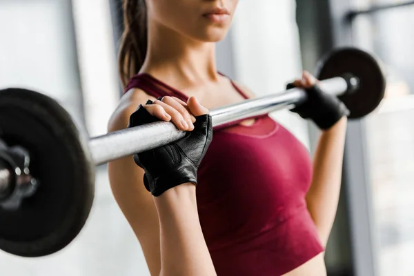 Vista recortada de la deportista concentrada en el entrenamiento de guantes de levantamiento de pesas con barra en el gimnasio - foto de stock