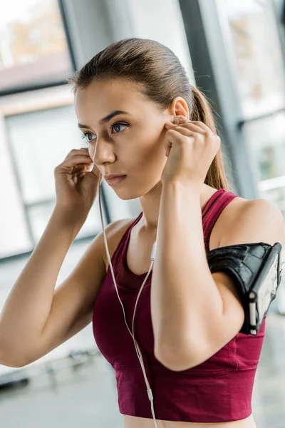 Porträt einer fitten Sportlerin mit Smartphone-Armbinde, die im Fitnessstudio Kopfhörer aufsetzt — Stockfoto