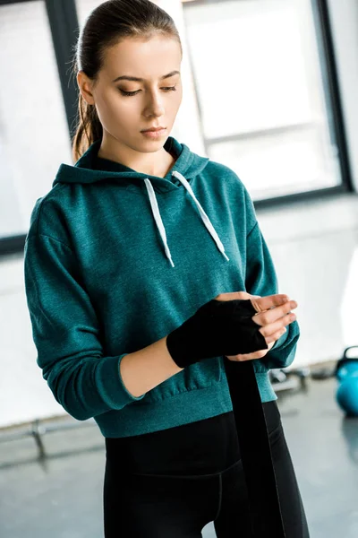 Hermosa deportista enfocada ponerse guantes deportivos en el gimnasio - foto de stock