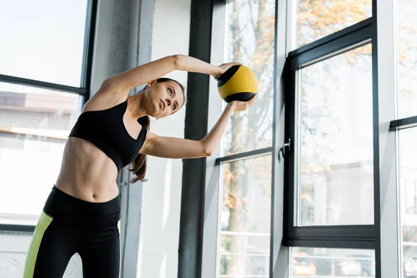 Beautiful fit sportswoman training and stretching with medicine ball at gym — Stock Photo