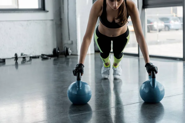 Determinada esportista em luvas de levantamento de peso fazendo exercício prancha em kettlebells no centro de esportes — Fotografia de Stock