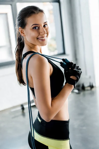 Porträt einer attraktiven Sportlerin, die in die Kamera blickt und im Fitnessstudio Springseil hält — Stockfoto