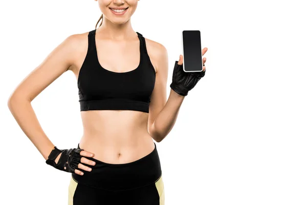 Vista recortada de la deportista en forma de guantes de levantamiento de pesas que sostiene el teléfono inteligente con pantalla en blanco aislado en blanco - foto de stock