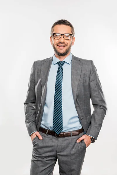 Hombre de negocios guapo en gafas de pie con las manos en los bolsillos y sonriendo a la cámara aislada en blanco - foto de stock