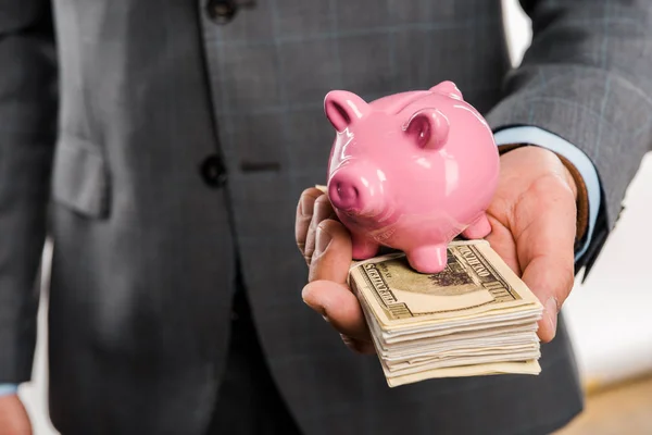 Close-up partial view of businessman holding dollar banknotes and piggy bank — Stock Photo