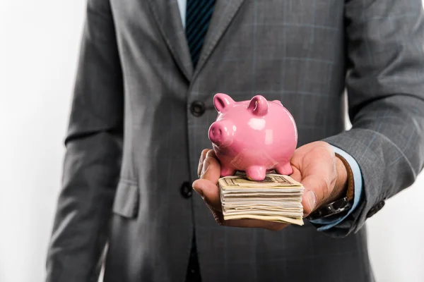 Close-up partial view of businessman holding piggy bank and dollar banknotes isolated on white — Stock Photo