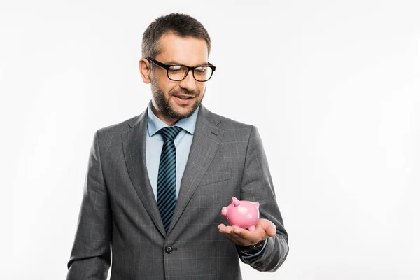 Bonito empresário em terno e óculos segurando porquinho banco isolado no branco — Fotografia de Stock