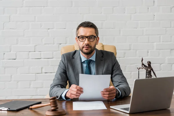 Seriöser Anwalt mit Brille, der mit Papieren arbeitet und im Büro in die Kamera schaut — Stockfoto