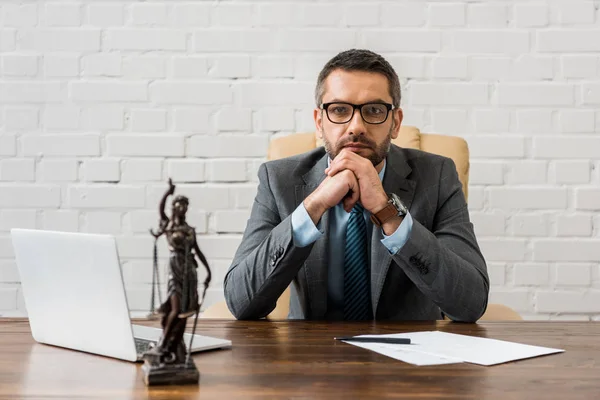 Sérieux barbu avocat en costume assis sur le lieu de travail et regardant la caméra — Photo de stock