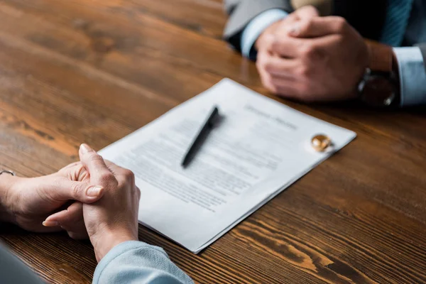 Vista parcial de abogado y cliente sentado en la mesa con el decreto de divorcio y anillos de boda - foto de stock