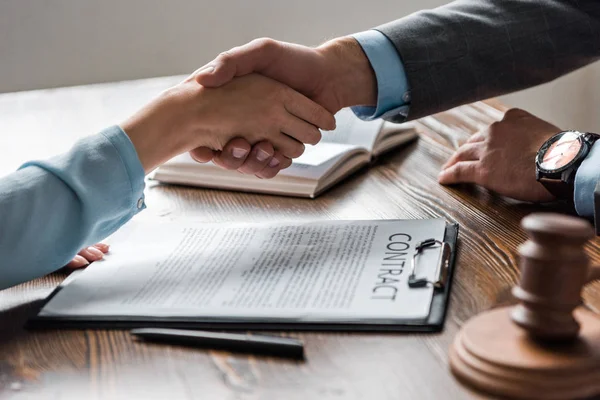 Обрезанный снимок с адвокатом и клиентом, пожимающими друг другу руки над контрактом — стоковое фото