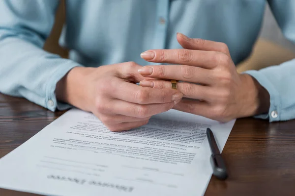 Corte tiro de mulher decolando anel de casamento e decreto de divórcio na mesa — Fotografia de Stock