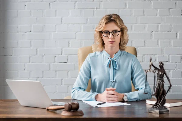 Серйозний жіночий адвокат в окулярах, сидячи на робочому місці і дивлячись на камеру — стокове фото