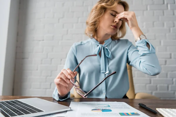 Vue à faible angle de la femme d'affaires fatiguée tenant des lunettes et frottant le nez pont sur le lieu de travail — Photo de stock