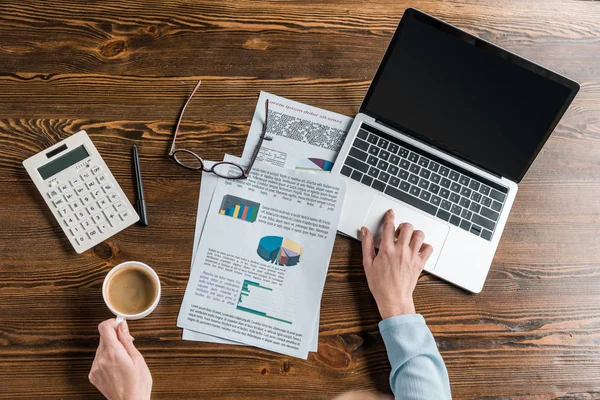 Vue partielle du dessus de la femme d'affaires en utilisant un ordinateur portable et tenant tasse de café — Photo de stock