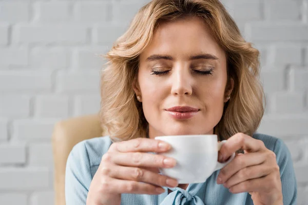 Mulher de negócios sorridente com olhos fechados segurando xícara de café no local de trabalho — Fotografia de Stock