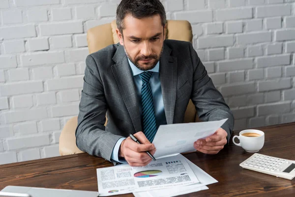 Guapo hombre de negocios concentrado haciendo papeleo en el lugar de trabajo - foto de stock