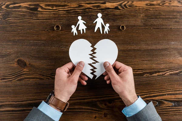 Abgeschnittene Aufnahme eines Mannes mit zerrissenem Herzen mit Familie und Verlobungsringen auf Holztisch, Scheidungskonzept — Stockfoto