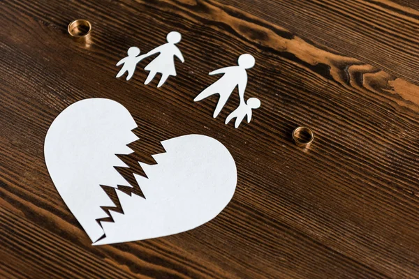 Close-up tiro de coração rasgado com família e anéis de noivado na mesa de madeira, conceito de divórcio — Fotografia de Stock