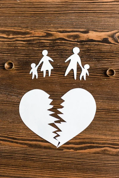 Vista superior do coração rasgado com família e anéis de noivado na mesa de madeira, conceito de divórcio — Fotografia de Stock