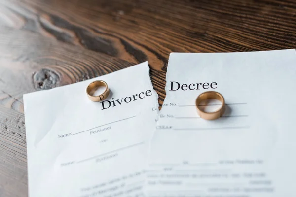 Close-up shot of teared divorce decree and engagement rings on wooden surface — Stock Photo