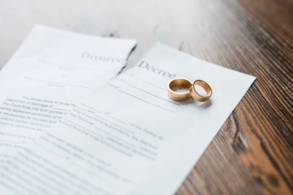 Close-up shot of teared divorce decree and engagement rings on wooden table — Stock Photo