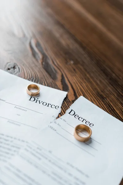 Close-up shot of teared divorce decree and engagement rings on wooden tabletop — Stock Photo