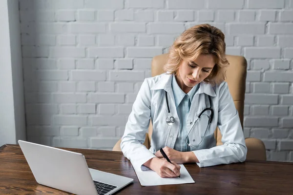 Confident female doctor writing document at workplace in office — Stock Photo