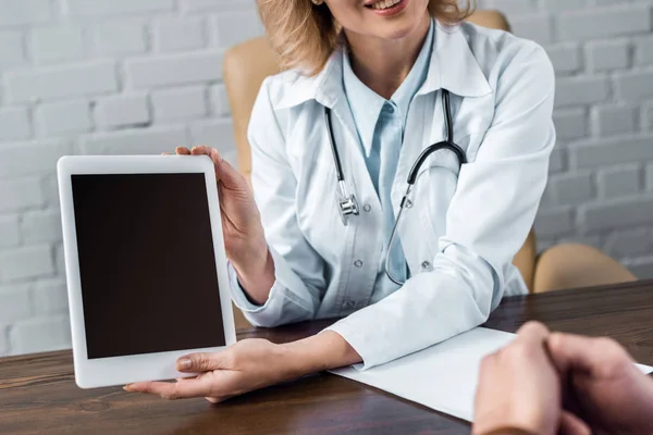 Recortado de médico femenino mostrando tableta con pantalla en blanco al paciente en el consultorio - foto de stock