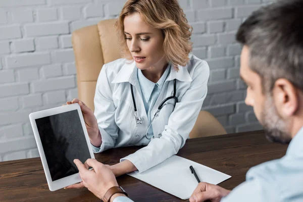 Attraente medico femminile che mostra tablet con schermo bianco al paziente in ufficio — Foto stock