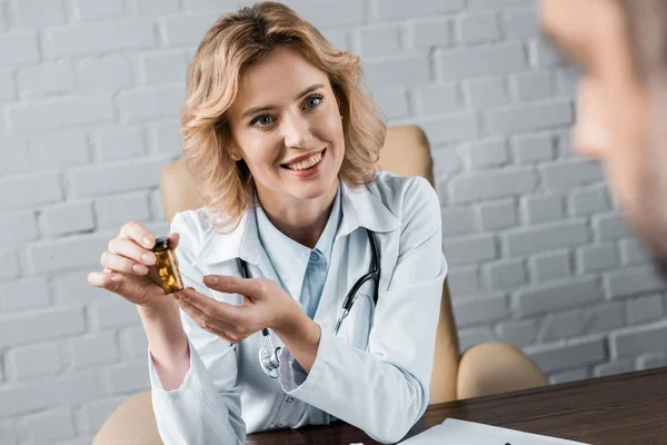 Привлекательная женщина-врач показывает банку с таблетками пациенту в офисе — стоковое фото